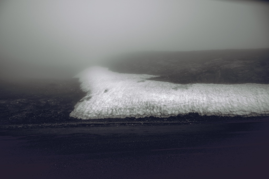 Brume — bande de neige persistante le long d’un sol sombre, paysage de montagne enveloppé de brouillard